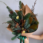 Bouquet of greenery with cinnamon sticks and lemons in brown paper packaging, held by a person.
