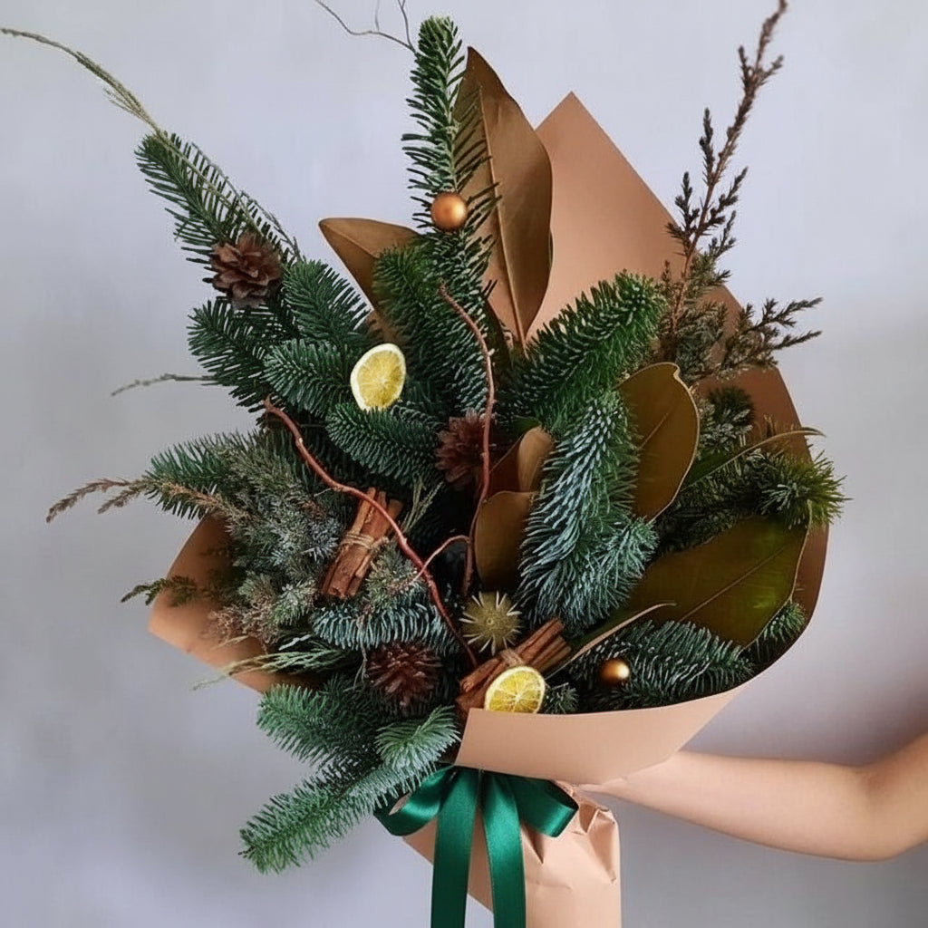 Bouquet of greenery with cinnamon sticks and lemons in brown paper packaging, held by a person.