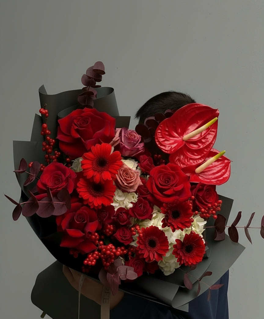 Bouquet of red and pink flowers held by a person against a gray background 