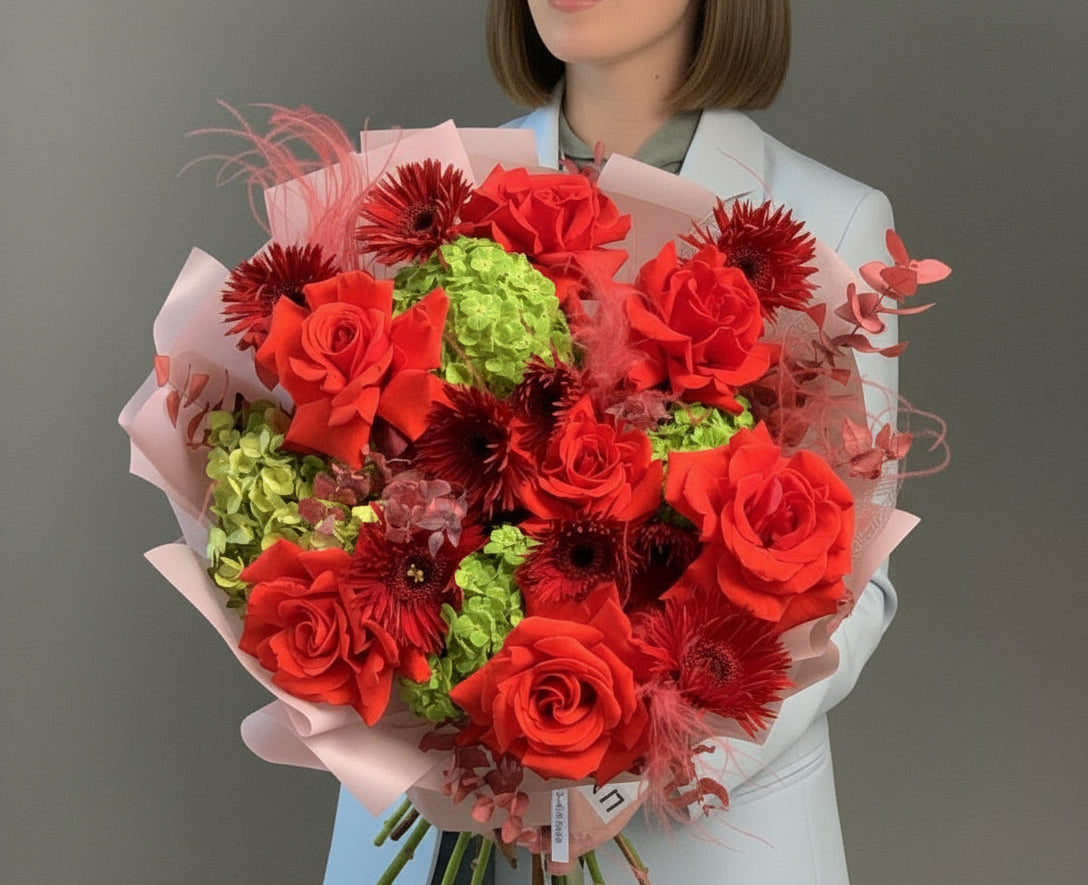 Bouquet of red and green flowers held by a person against a gray background