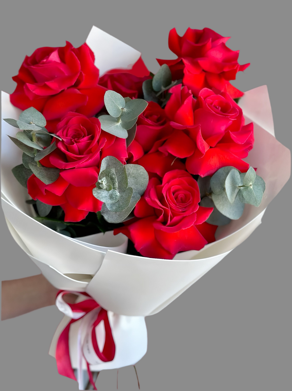Bouquet of red roses with greenery wrapped in white paper and ribbon 