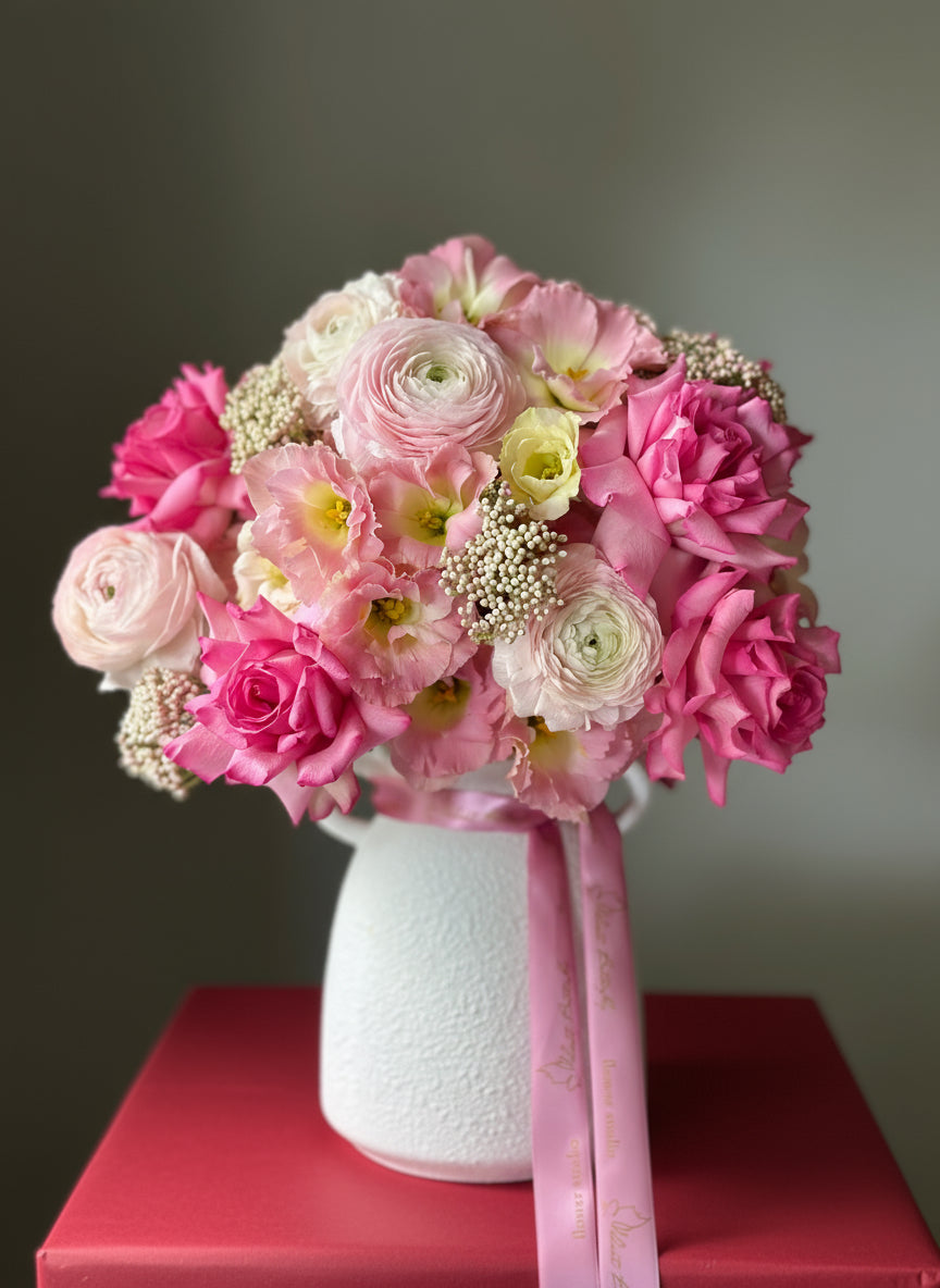 Bouquet of pink and white flowers in a white vase with a pink ribbon.