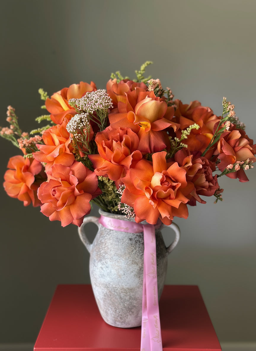 Bouquet of orange flowers in a textured vase with a pink ribbon.